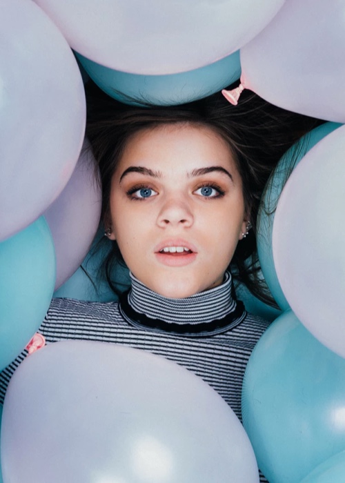 A photo of Harper surrounded by pastel blue and pink balloons.